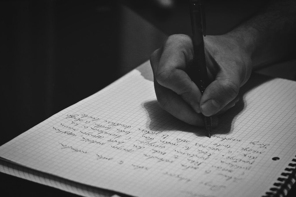 Hand writing in a notebook on a wooden desk